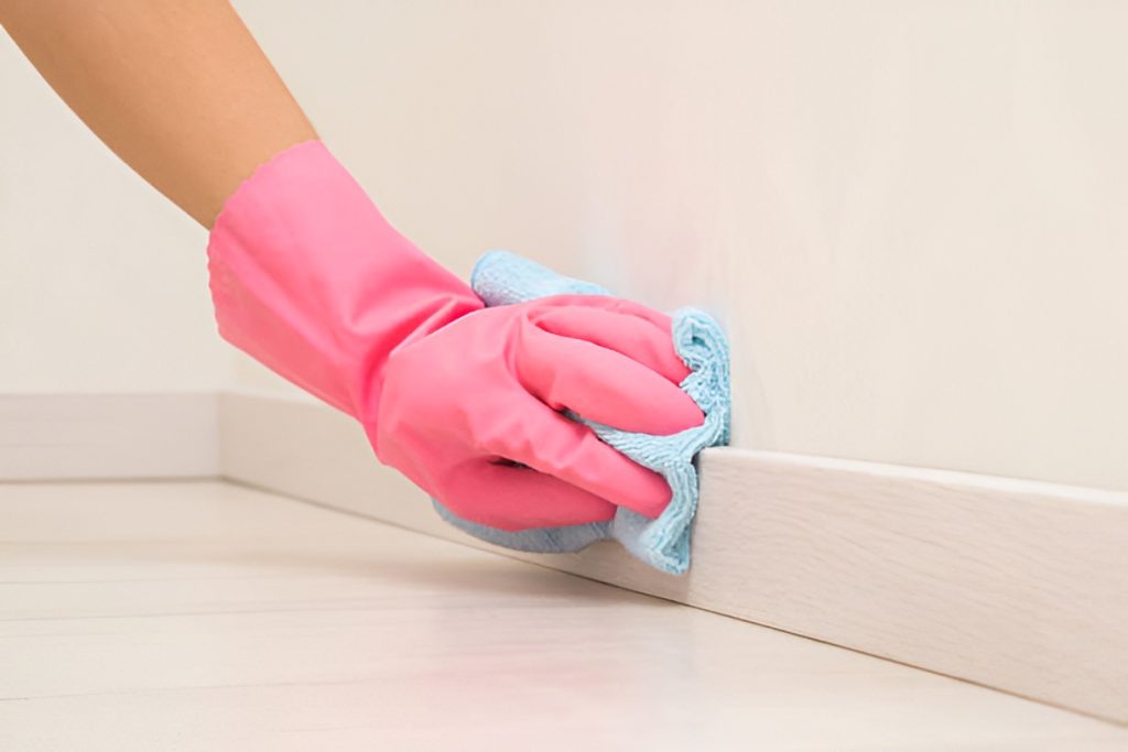 close-up of hand in a pink rubber glove cleaning a baseboard