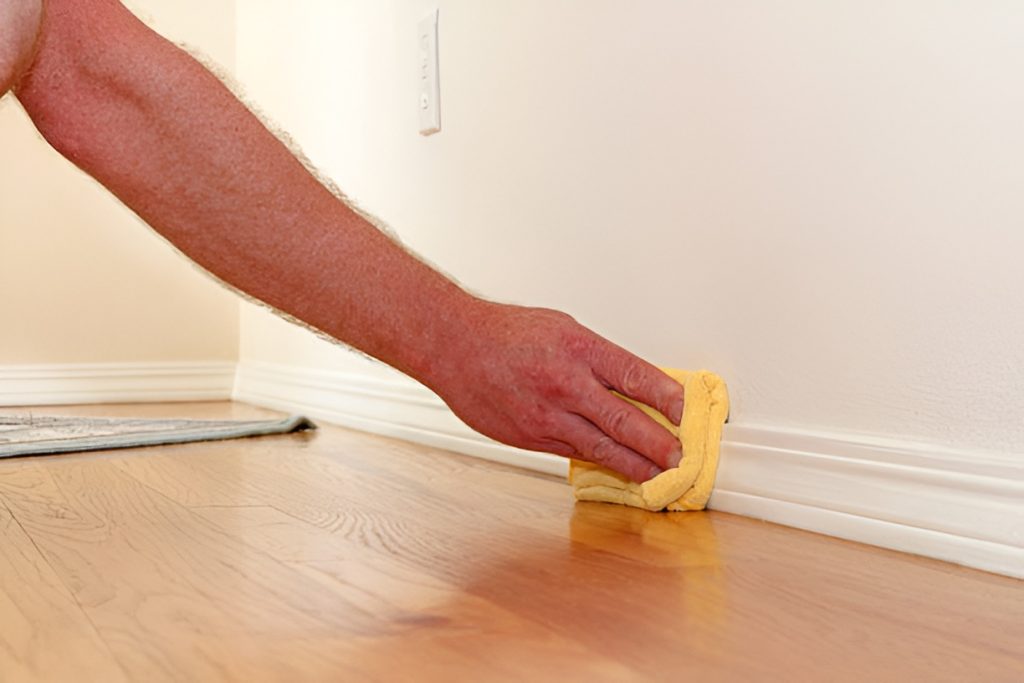 man cleaning a painted baseboard with a yellow microfiber cloth